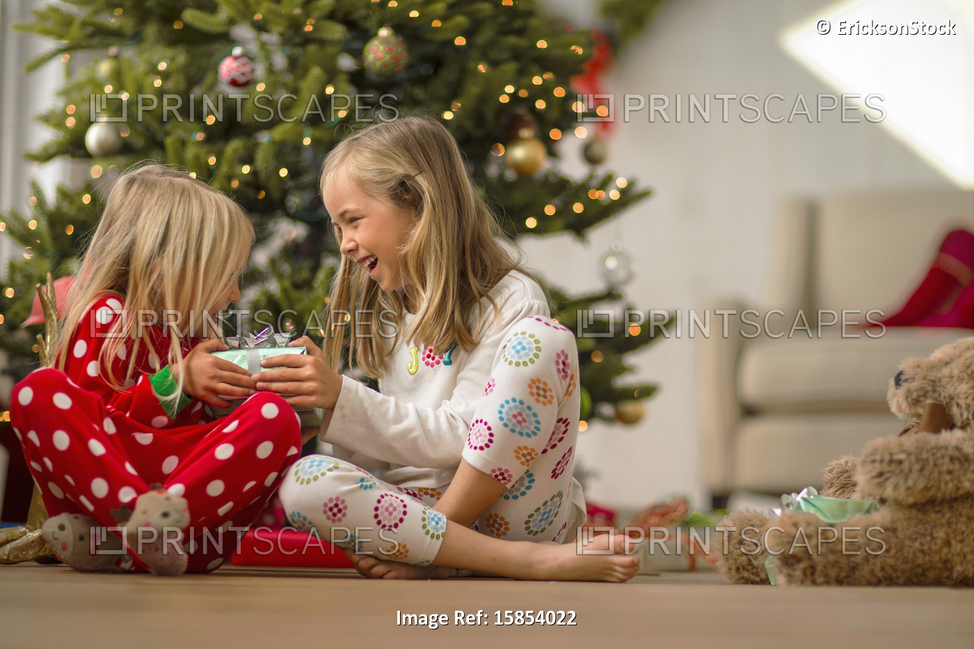 Two excited young sisters holding a present on Christmas morning.