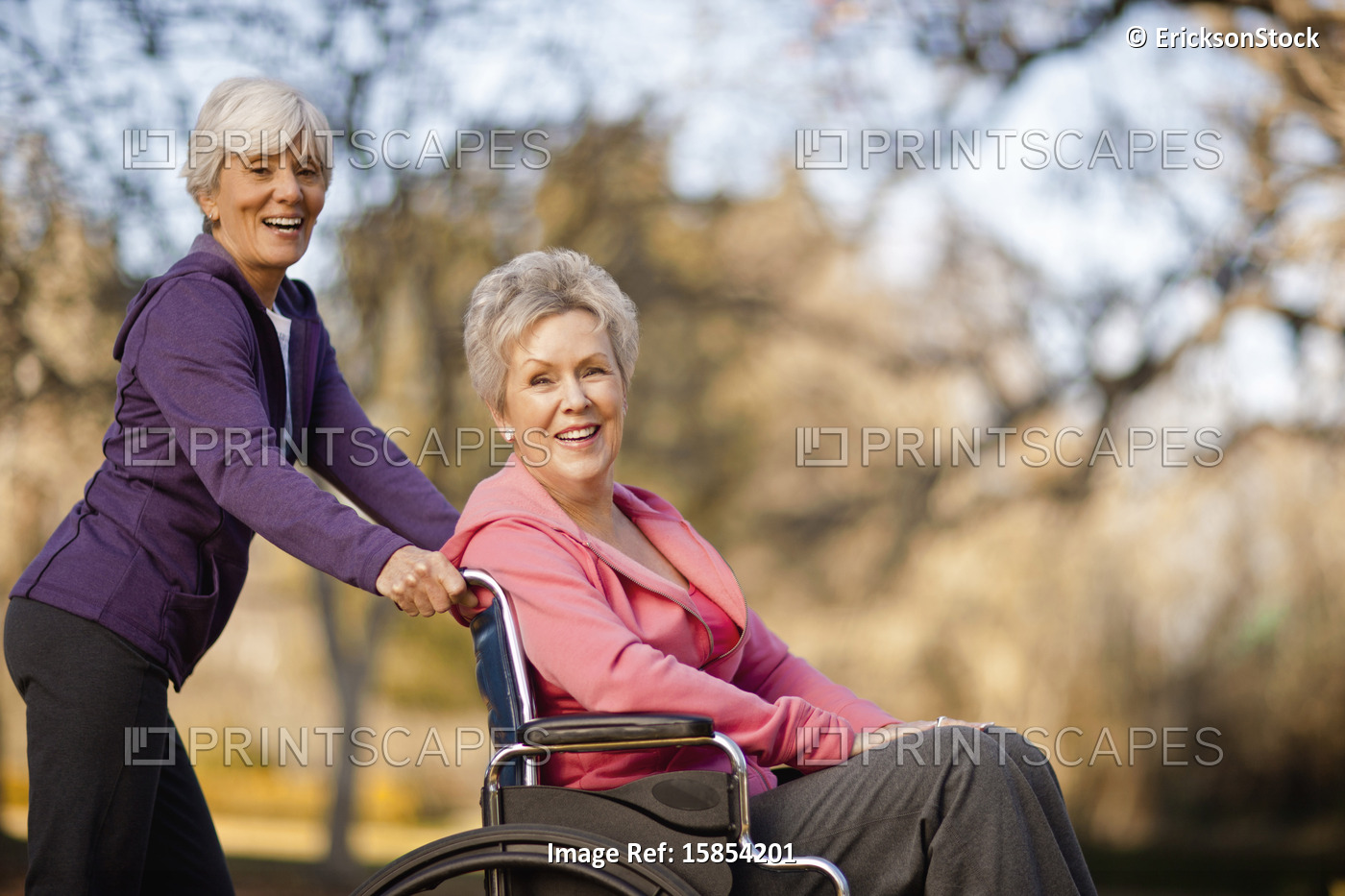 Portrait of a smiling senior woman being pushed through a park in a wheelchair ...