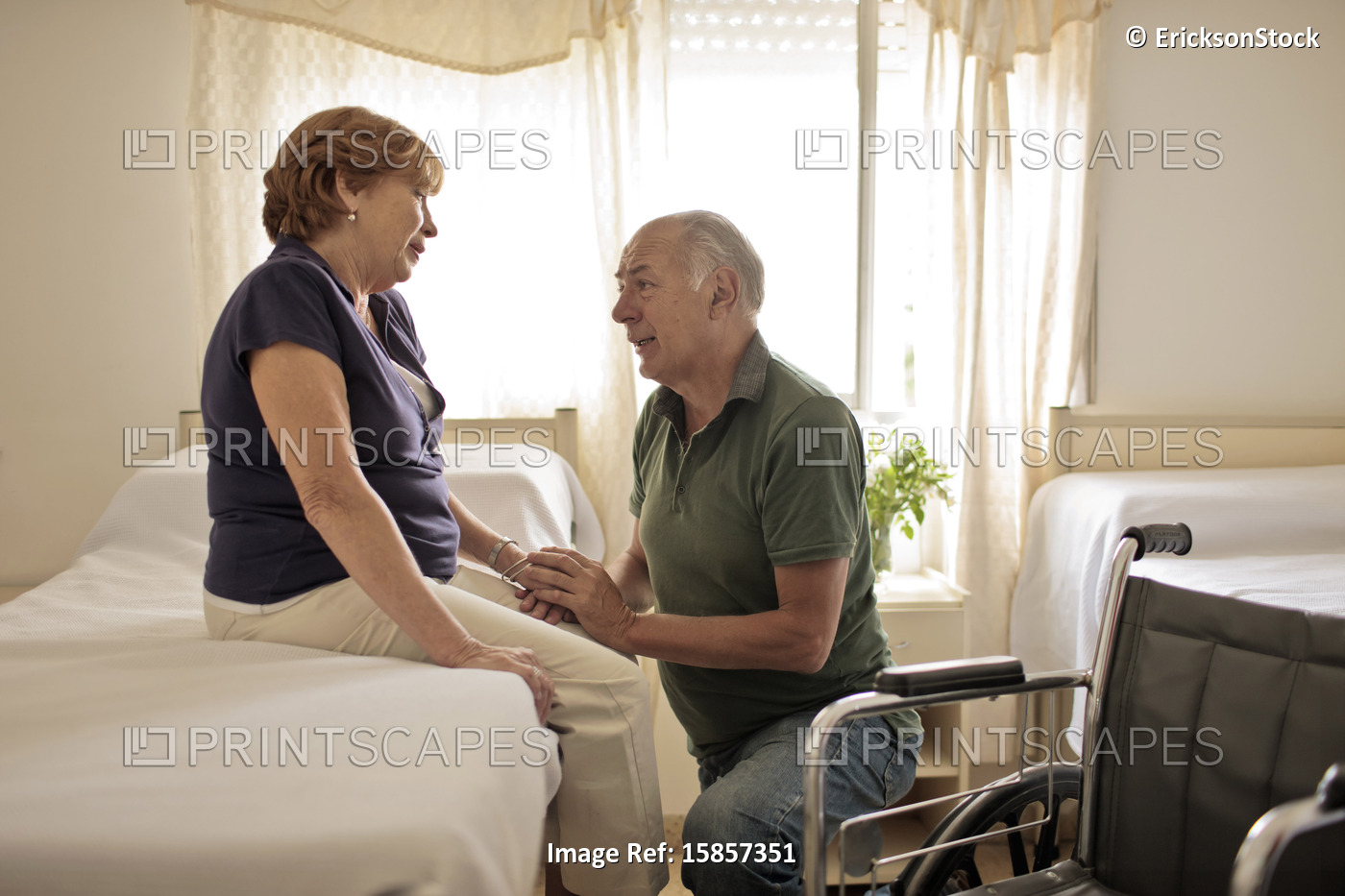Mature female patient sitting on hospital bed, her husband kneeling beside her ...