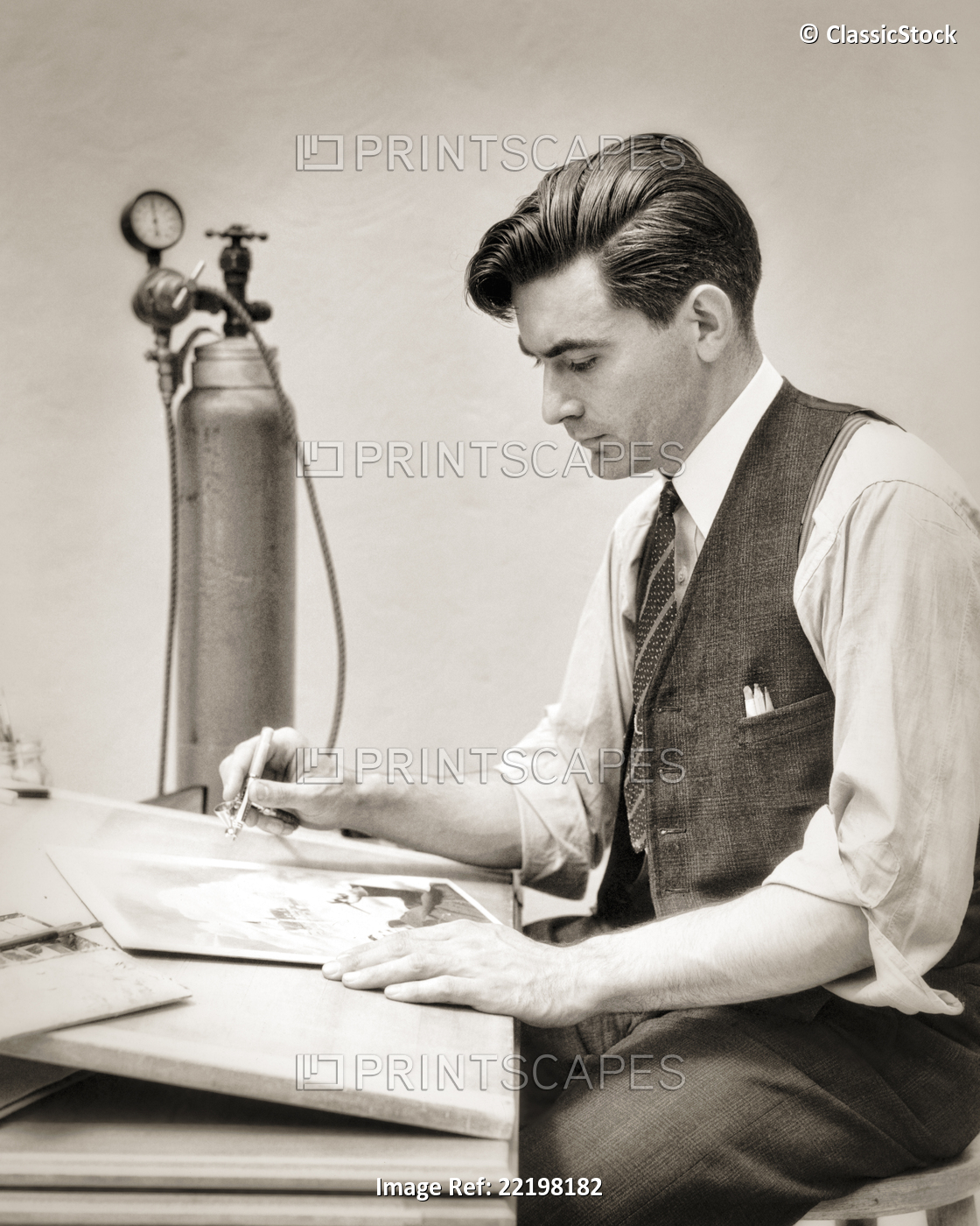 1930s MAN GRAPHIC ARTIST AIRBRUSHING A PHOTOGRAPH SEATED AT DESK BESIDE ...