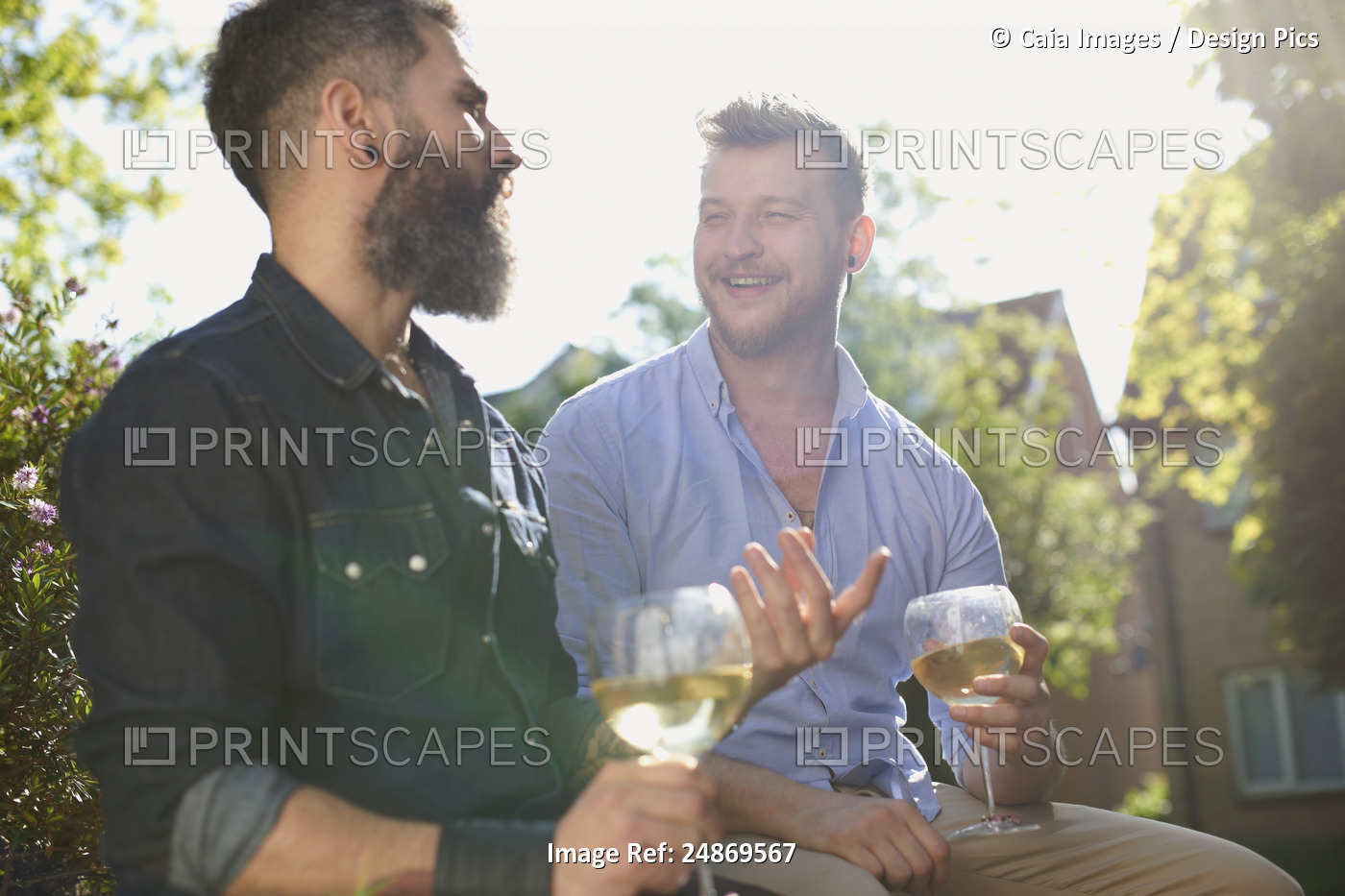 Smiling male gay couple drinking white wine in sunny garden