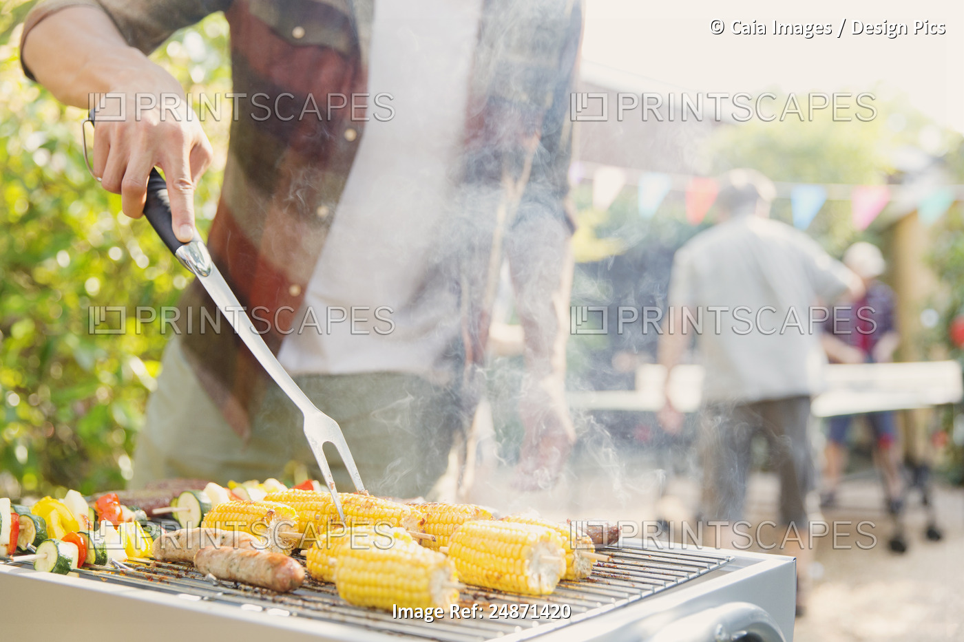 Man barbecuing corn, sausage and vegetable kebabs