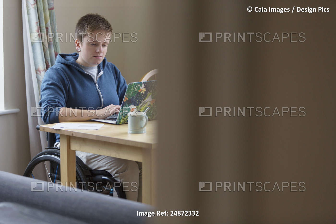 Young woman in wheelchair using laptop at dining table