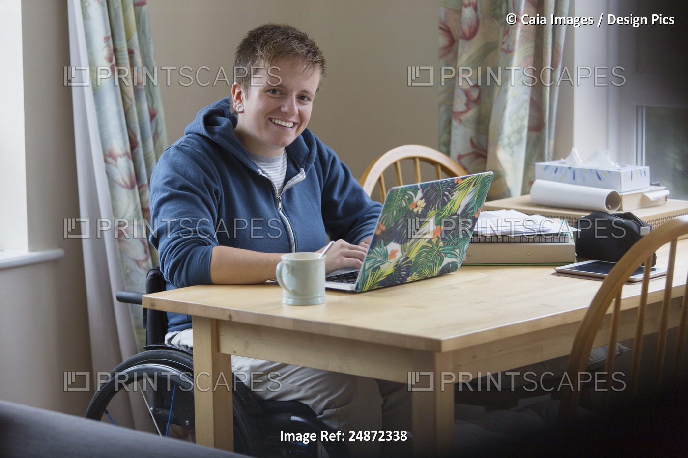 Portrait smiling, confident young woman in wheelchair using laptop at dining ...