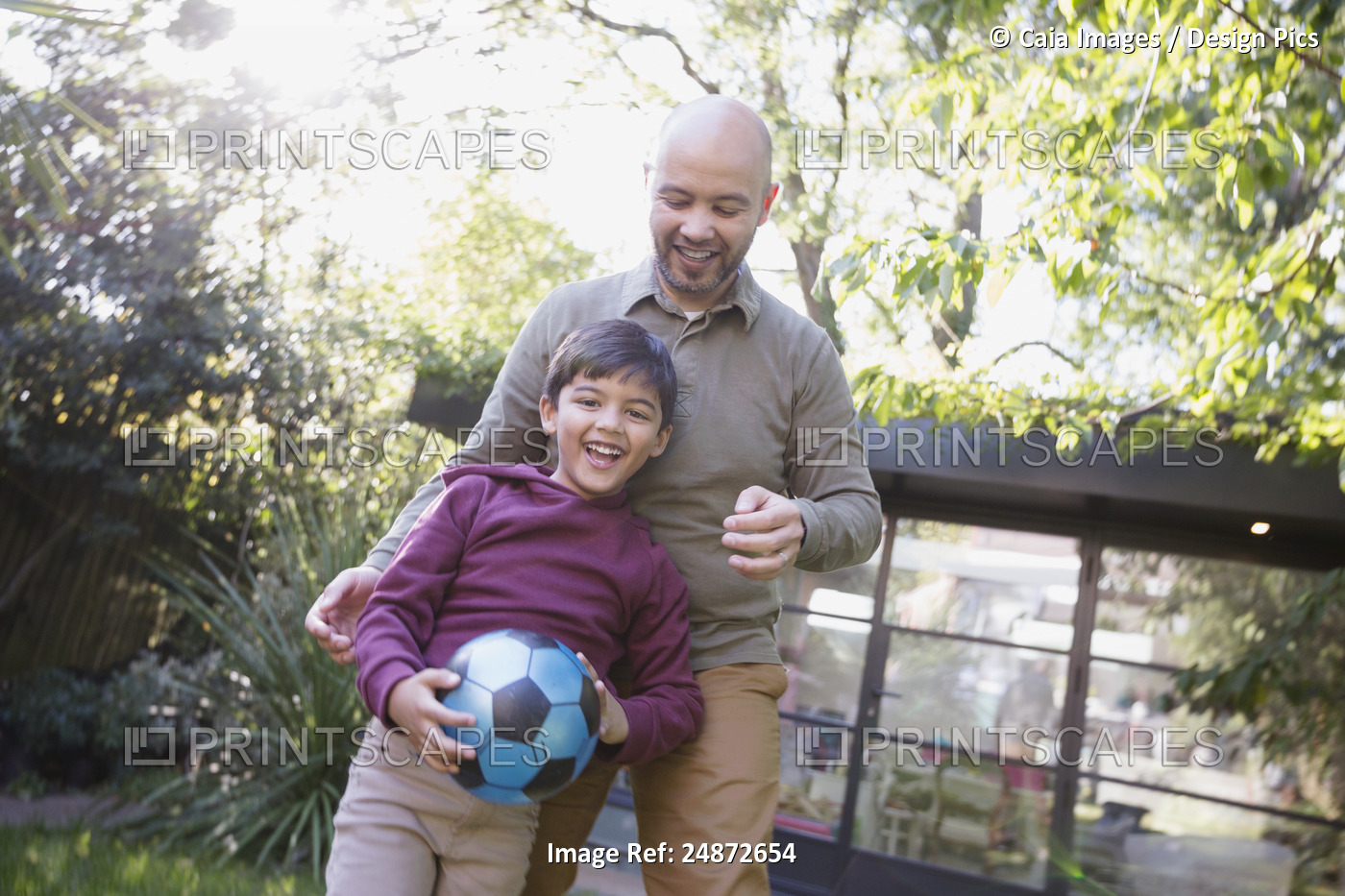 Father and son playing with soccer ball in backyard