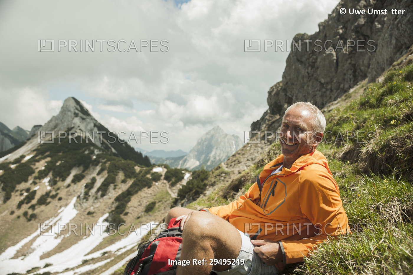 Portrait of mature man sitting on grass, hiking in mountains, Tannheim Valley, ...