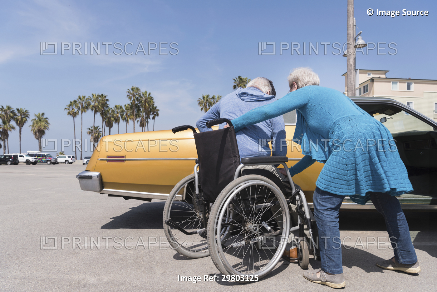 Senior woman helping husband in wheelchair by vintage car at Venice Beach, ...