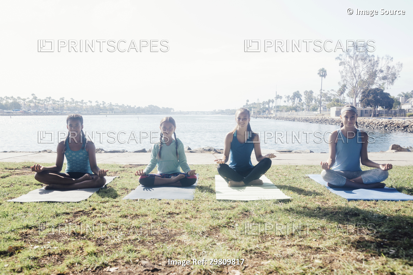 Schoolgirls practicing yoga lotus pose by lakeside on school sports field