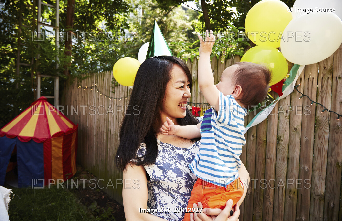 Mother wearing party hat holding baby boy at birthday party