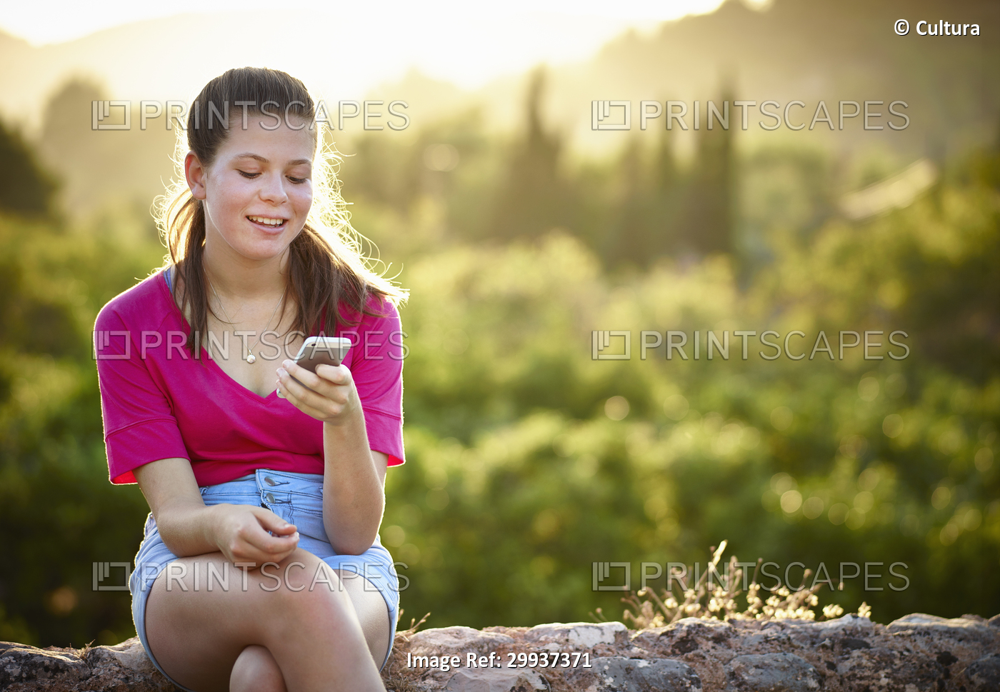 Teenage girl sitting on stone wall looking at smartphone, Majorca, Spain