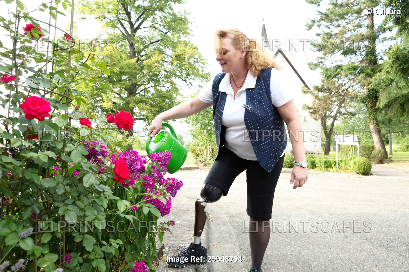Mid adult woman with prosthetic leg, in garden, watering plants