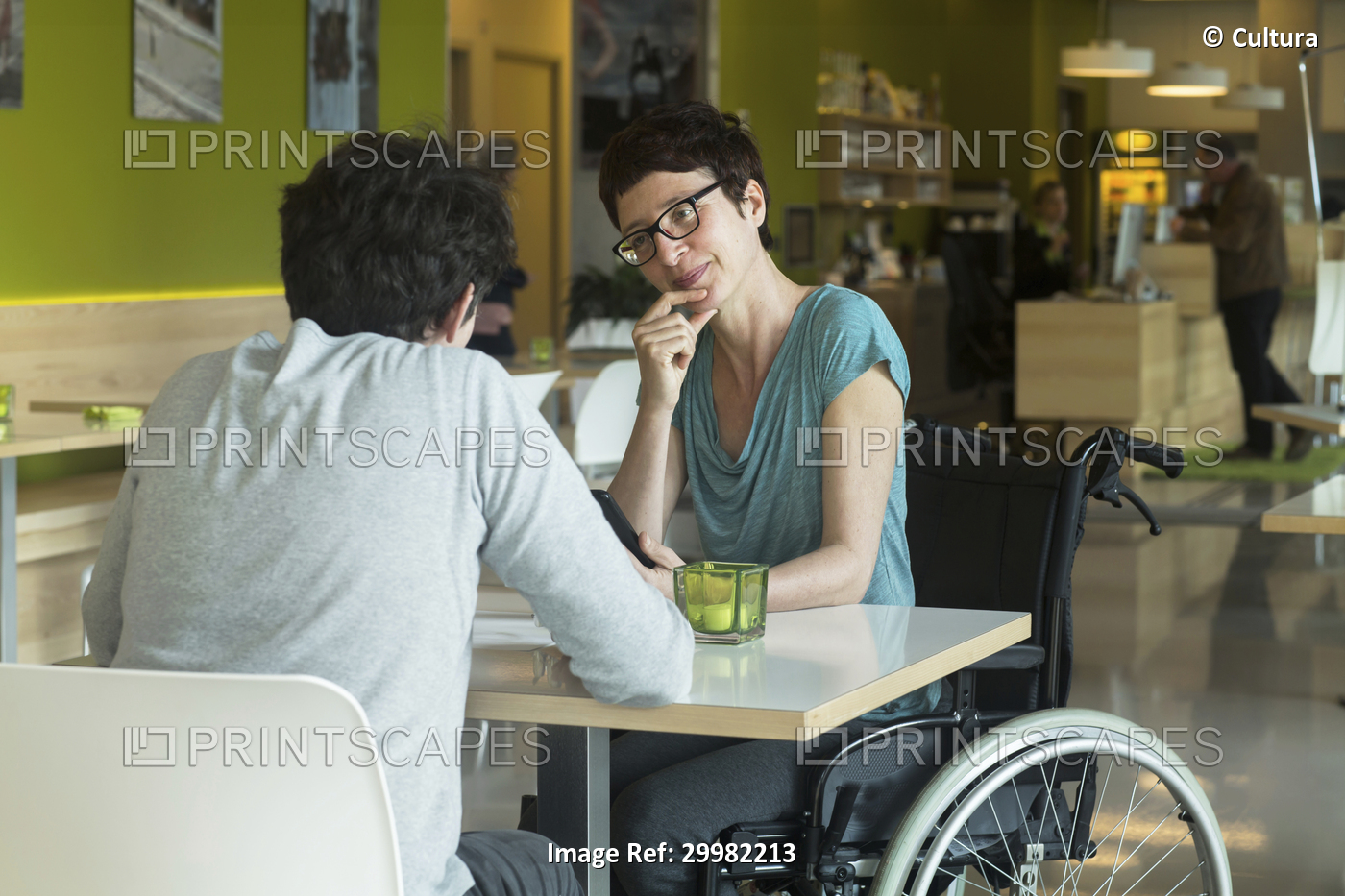 Woman in wheelchair, sitting at restaurant table with friend