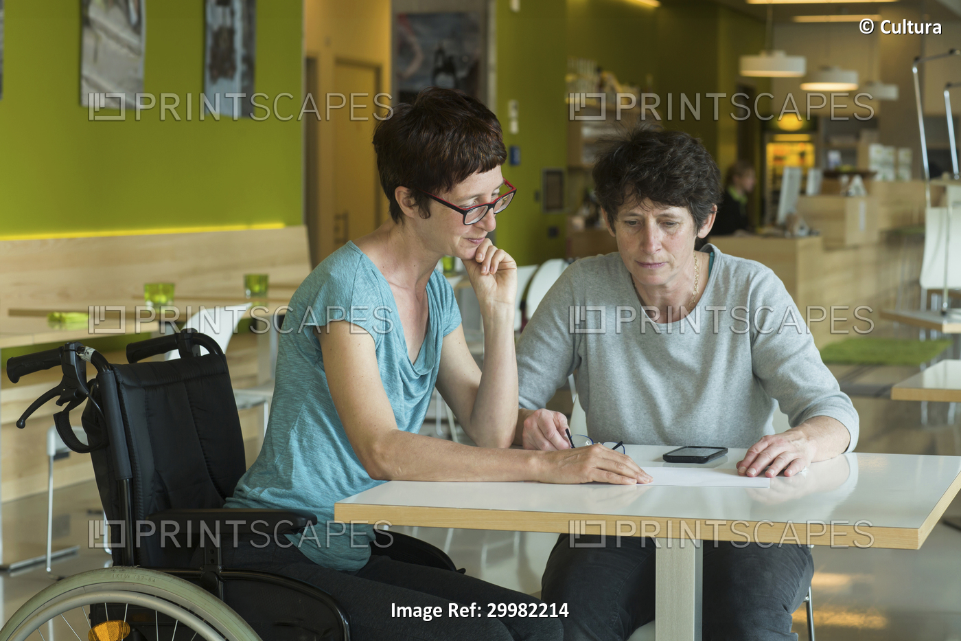 Woman in wheelchair, sitting at restaurant table, in discussion with friend