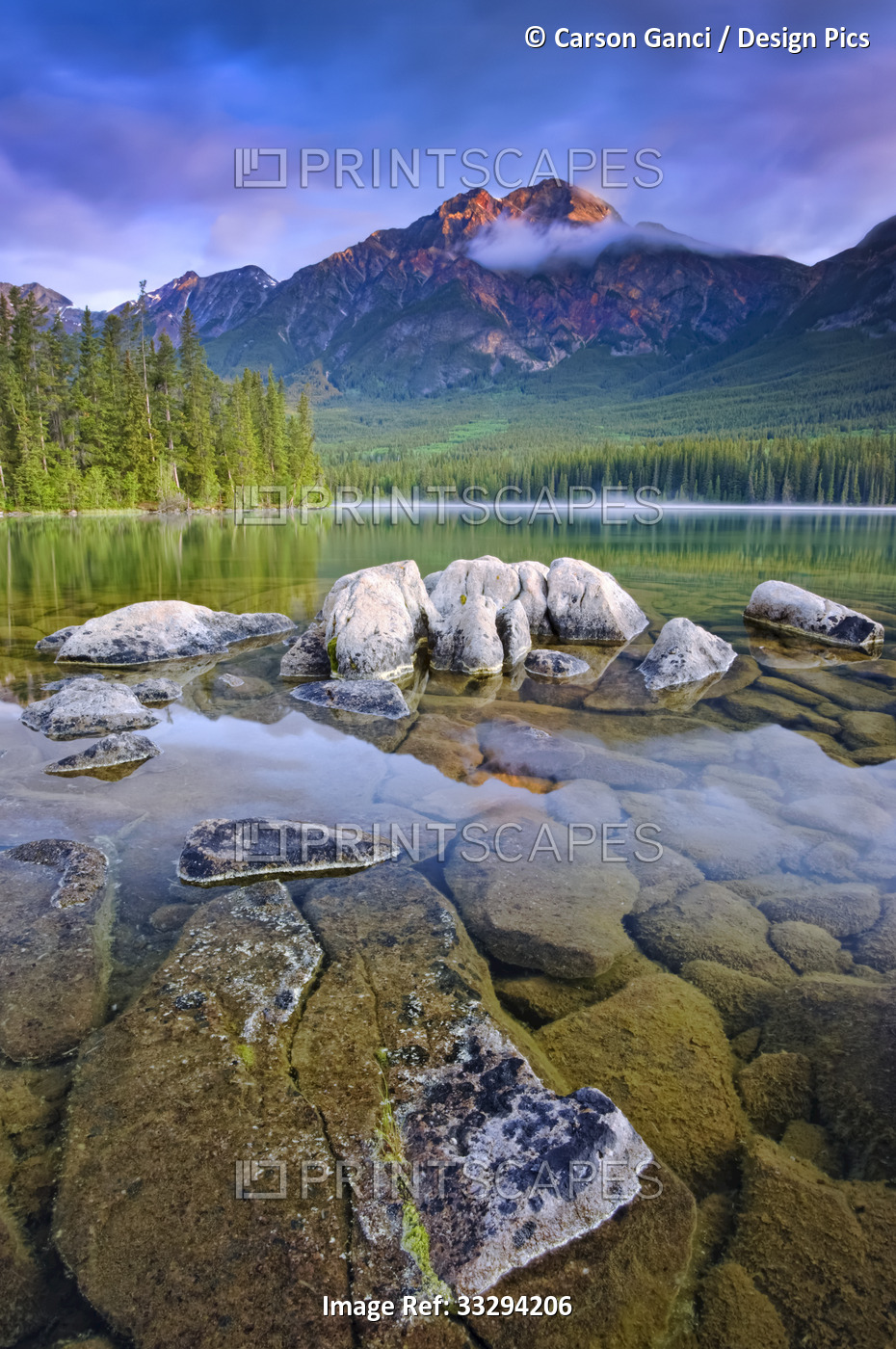 Morning glow on the rugged Rocky mountains with clear, tranquil lake water in ...