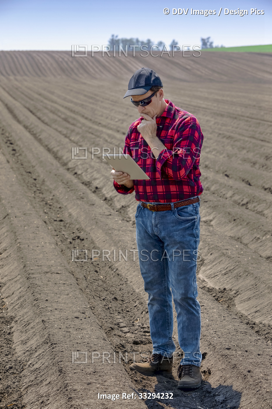 A farmer stands using a tablet on freshly tilled farmland; Alberta, Canada