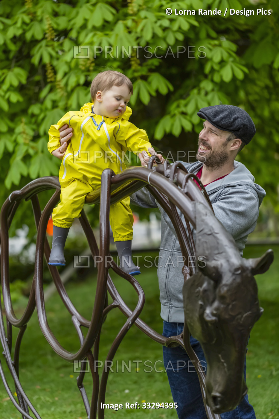 Close-up of father holding onto daughter sitting on top of horse sculpture in ...