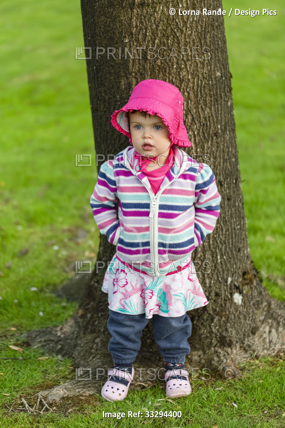 Portrait of young girl wearing colorful outfit standing in front of a tree in ...