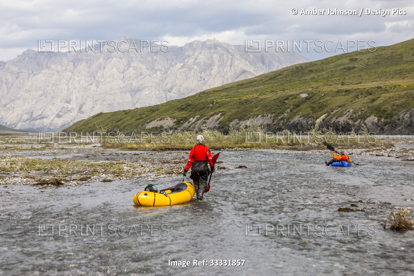 Caucasian woman wearing red drysuit, drags her yellow packraft down a shallow ...