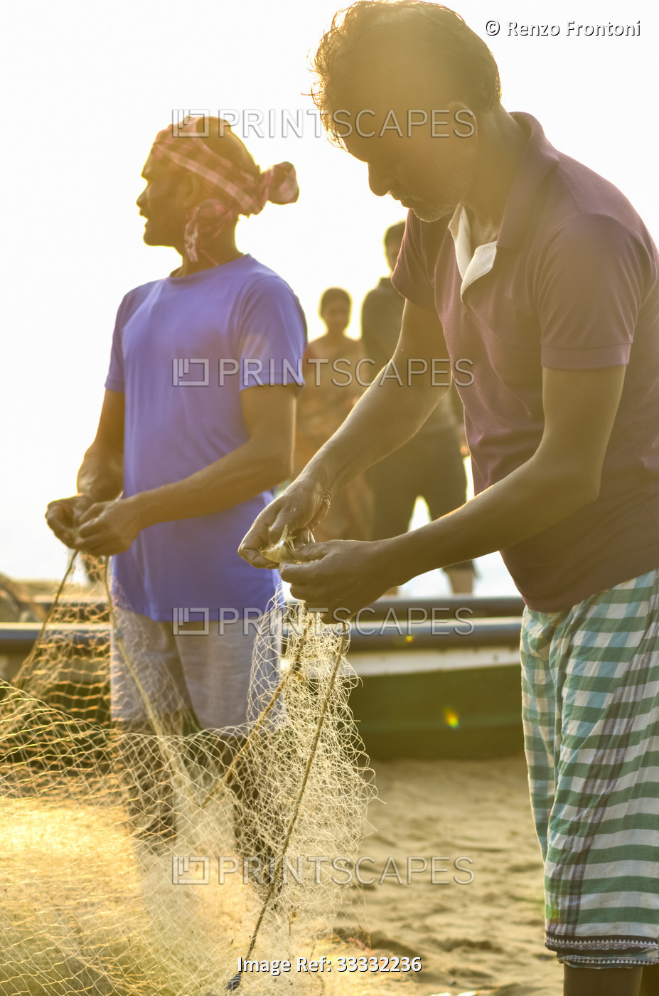 Fishermen standing in a boat on the waterfront cleaning a fishing net at Puri ...