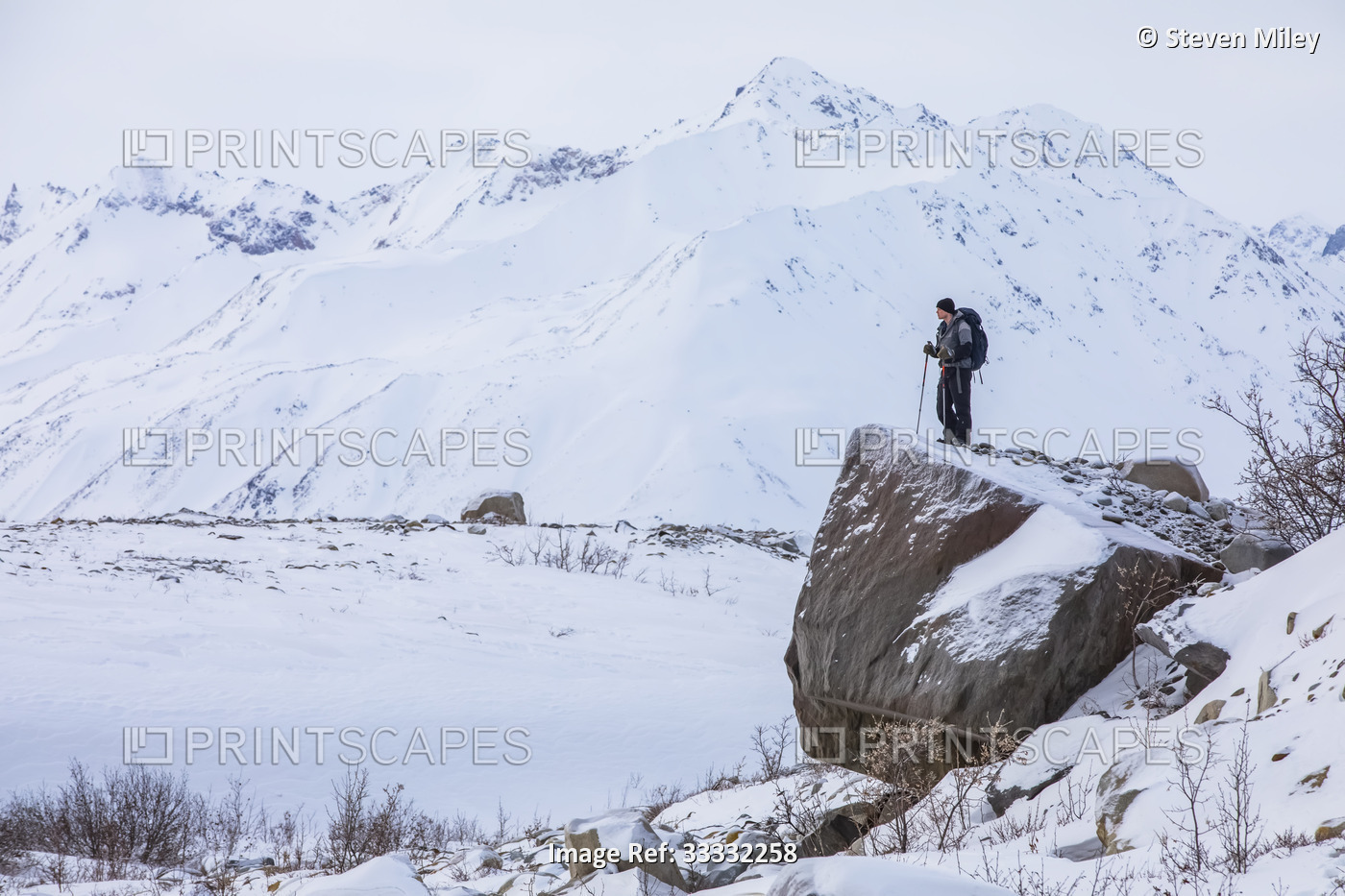 Man hiker stands on an erratic glacial-deposited rock from the retreat of the ...