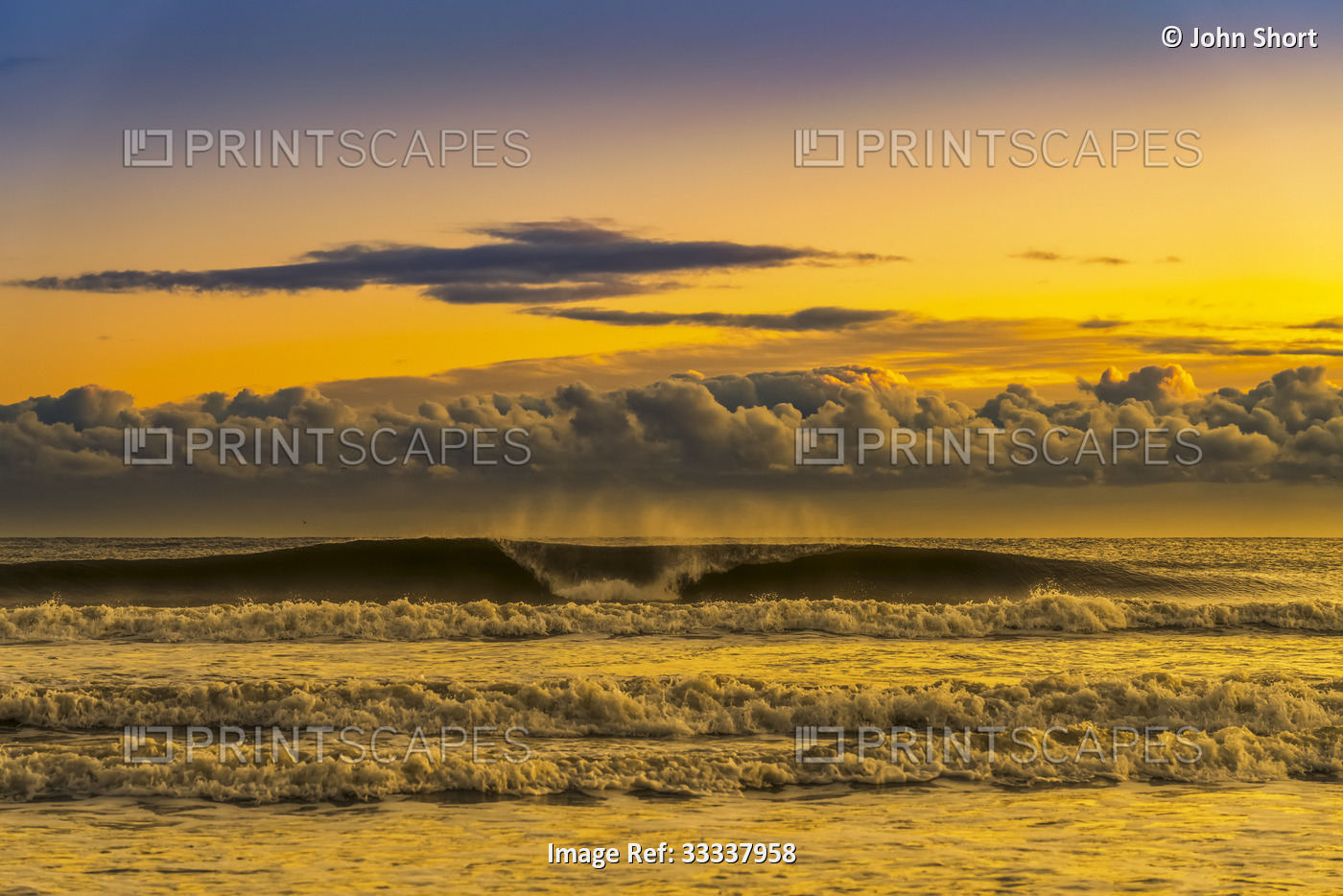 View of breaker waves and surf with low lying clouds in the sky at sunset; ...