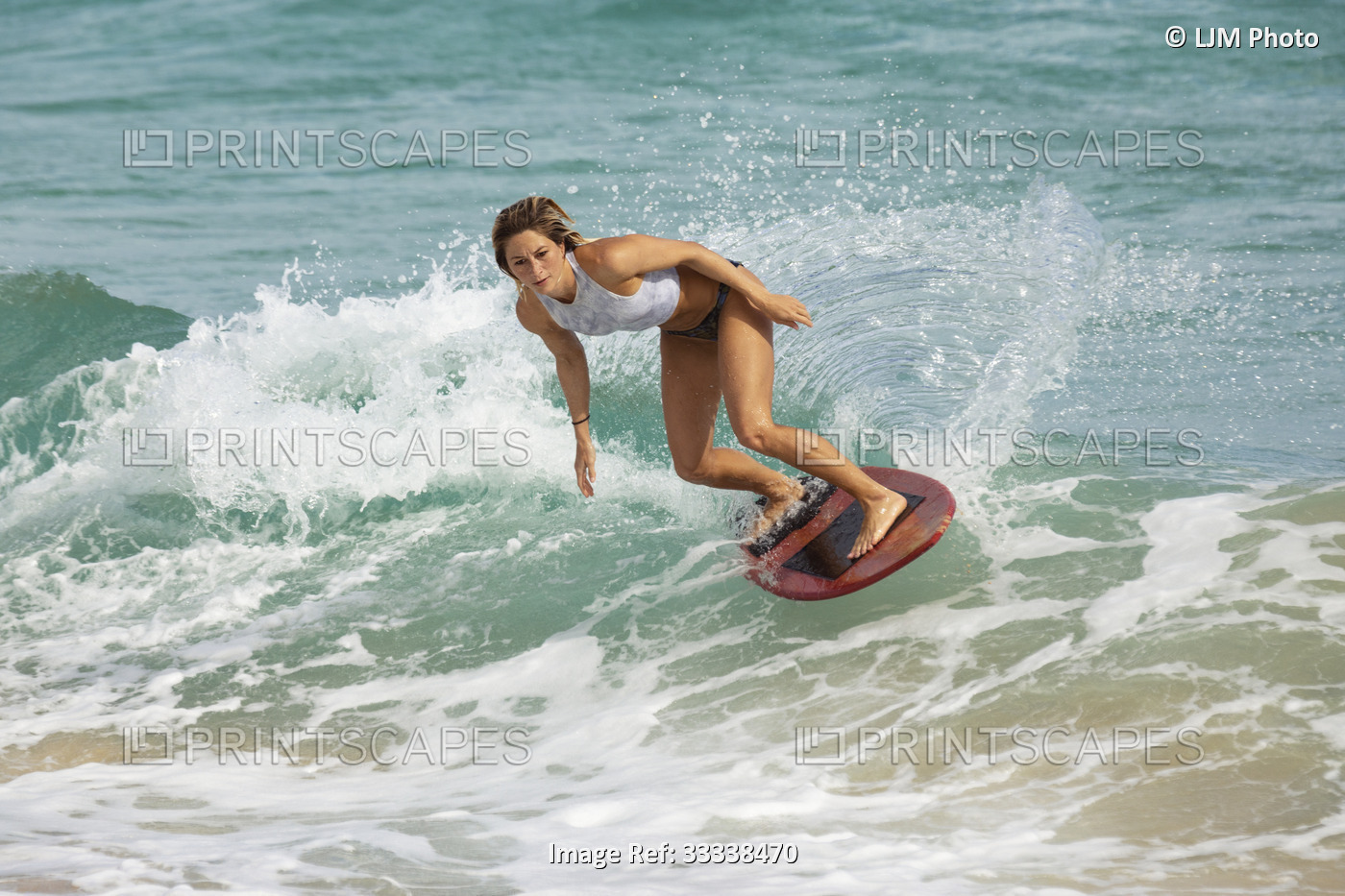 A young professional skimboarder riding the crest of a a wave at Sandy Beach; ...
