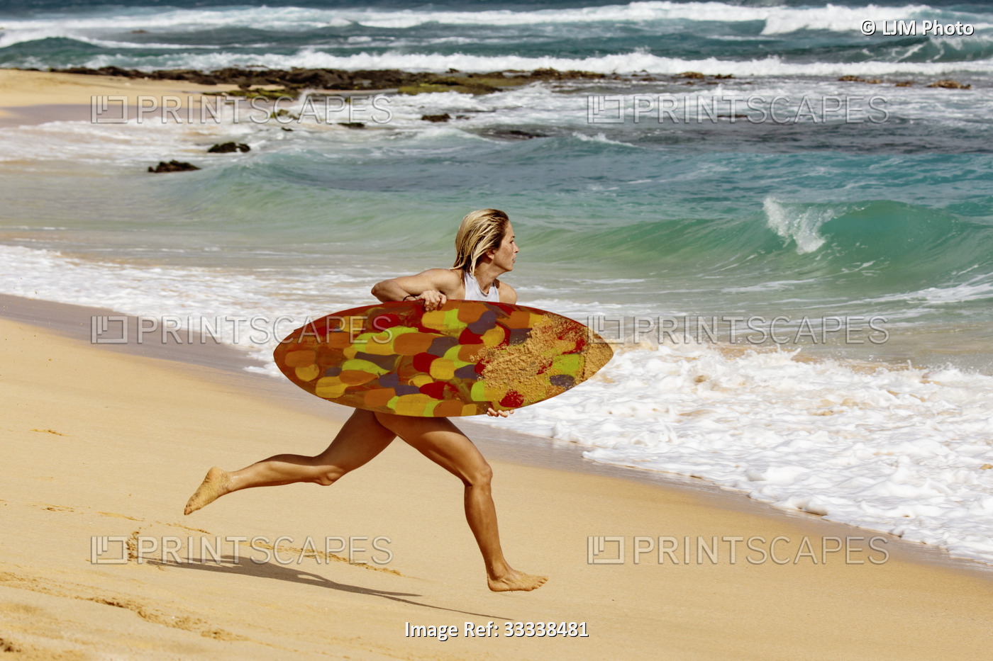 A young professional skimboarder running into a wave from the shore at Sandy ...