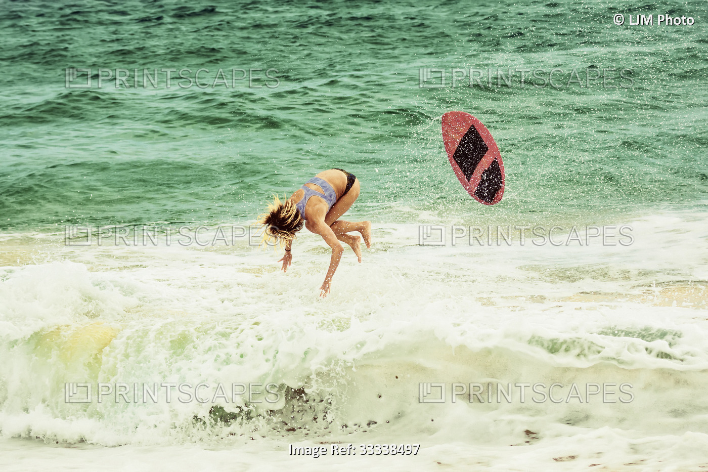 A young professional skimboarder wiping out while riding a wave at Sandy Beach; ...