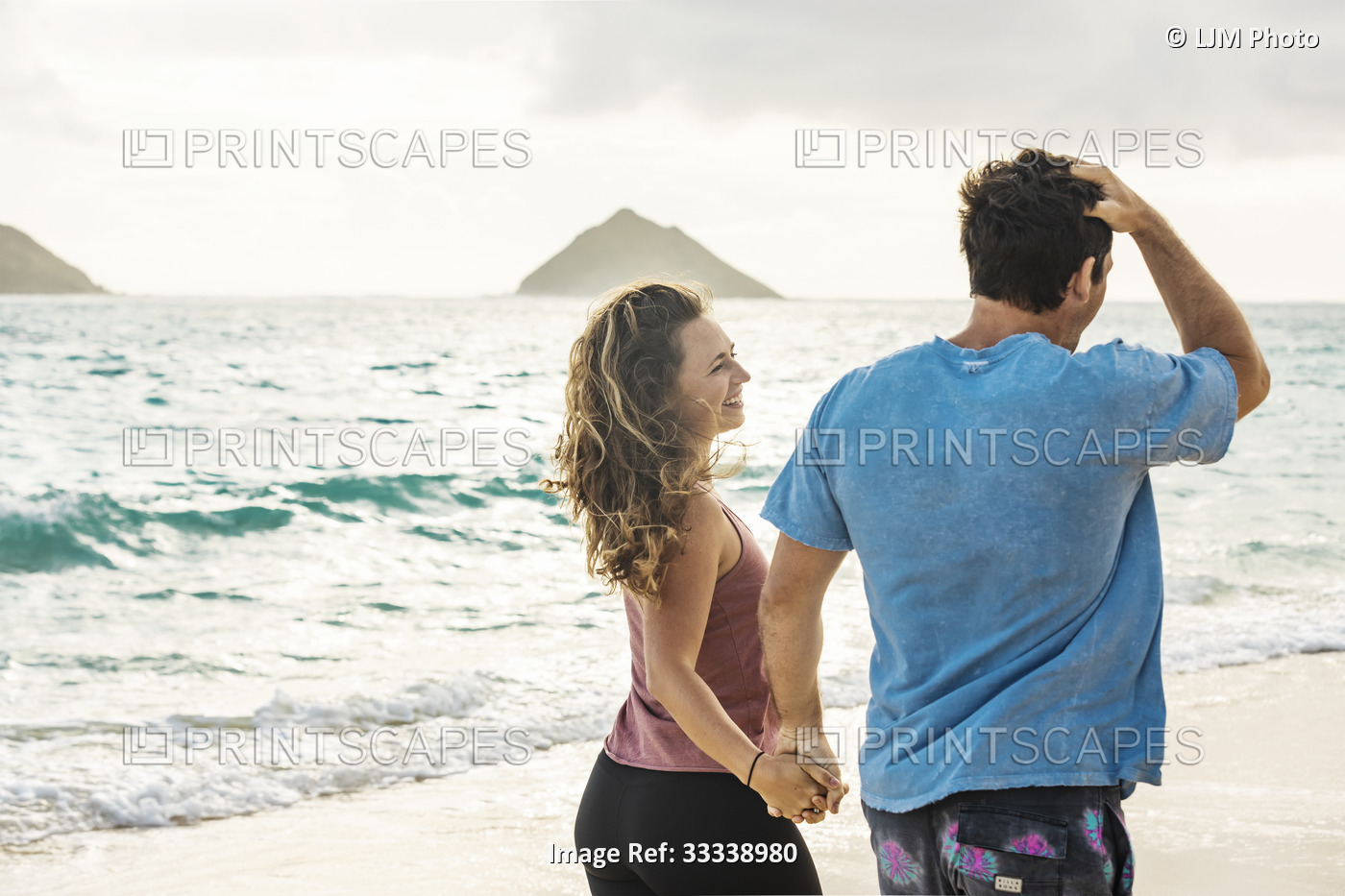 A view taken from behind of a millennial couple walking along Lanikai Beach ...