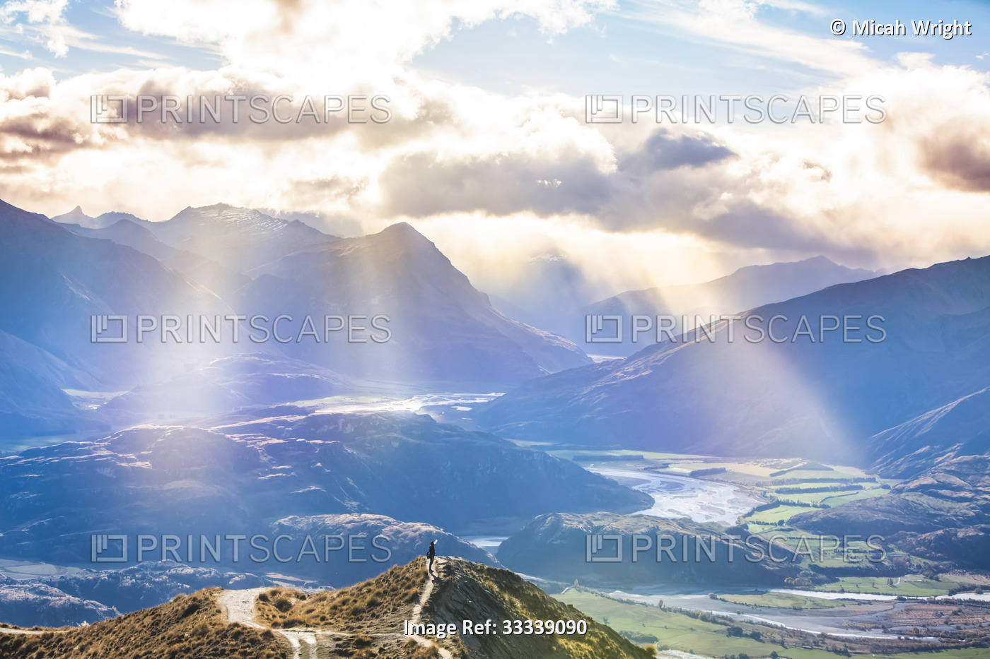 Man standing on mountaintop at Roys Peak with beautiful rays of sunlight after ...