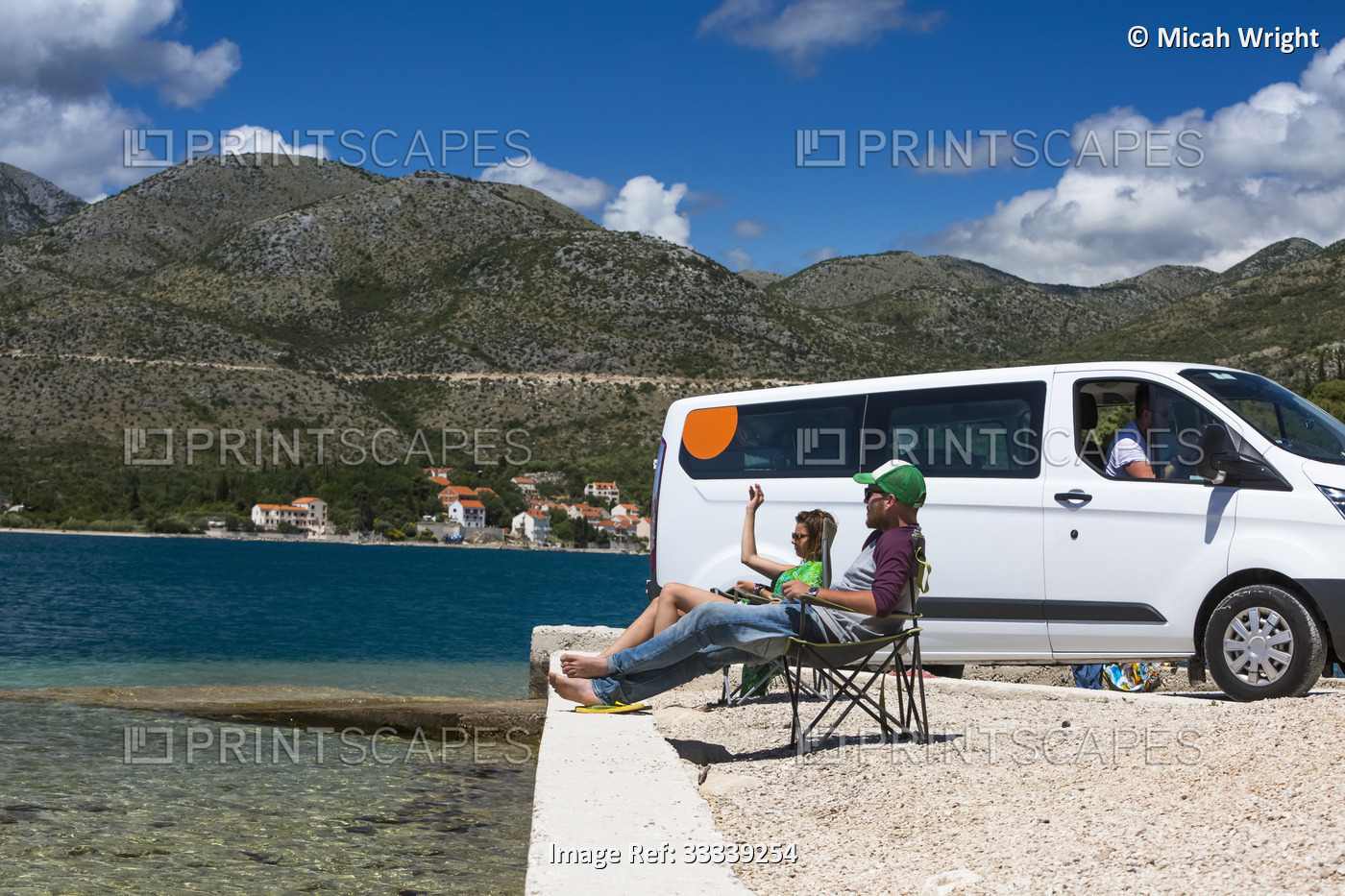 Friends sitting in the sun resting outside of a camper van as group of ...