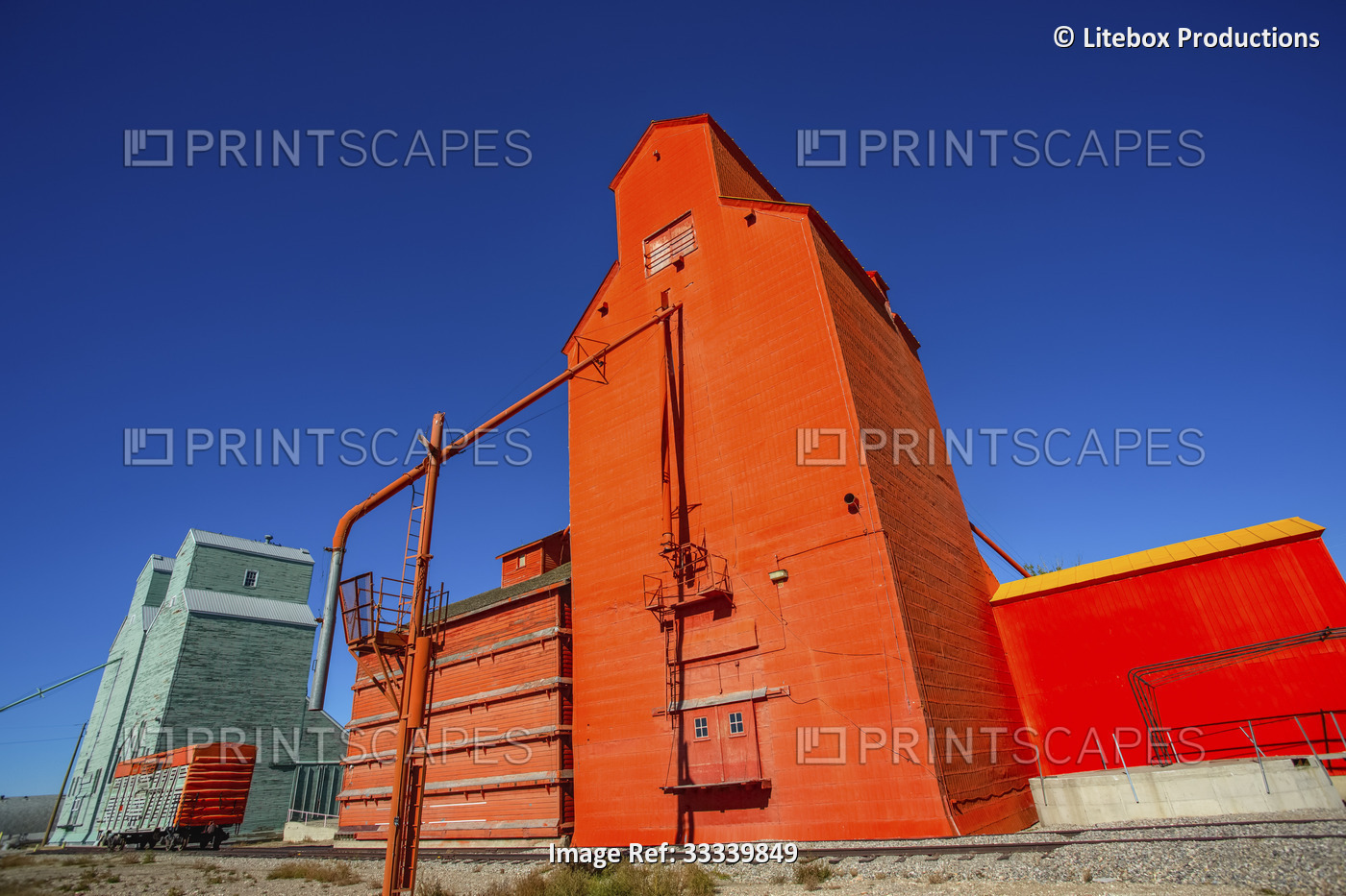 Orange grain elevator and rail car on tracks against a bright blue sky; ...