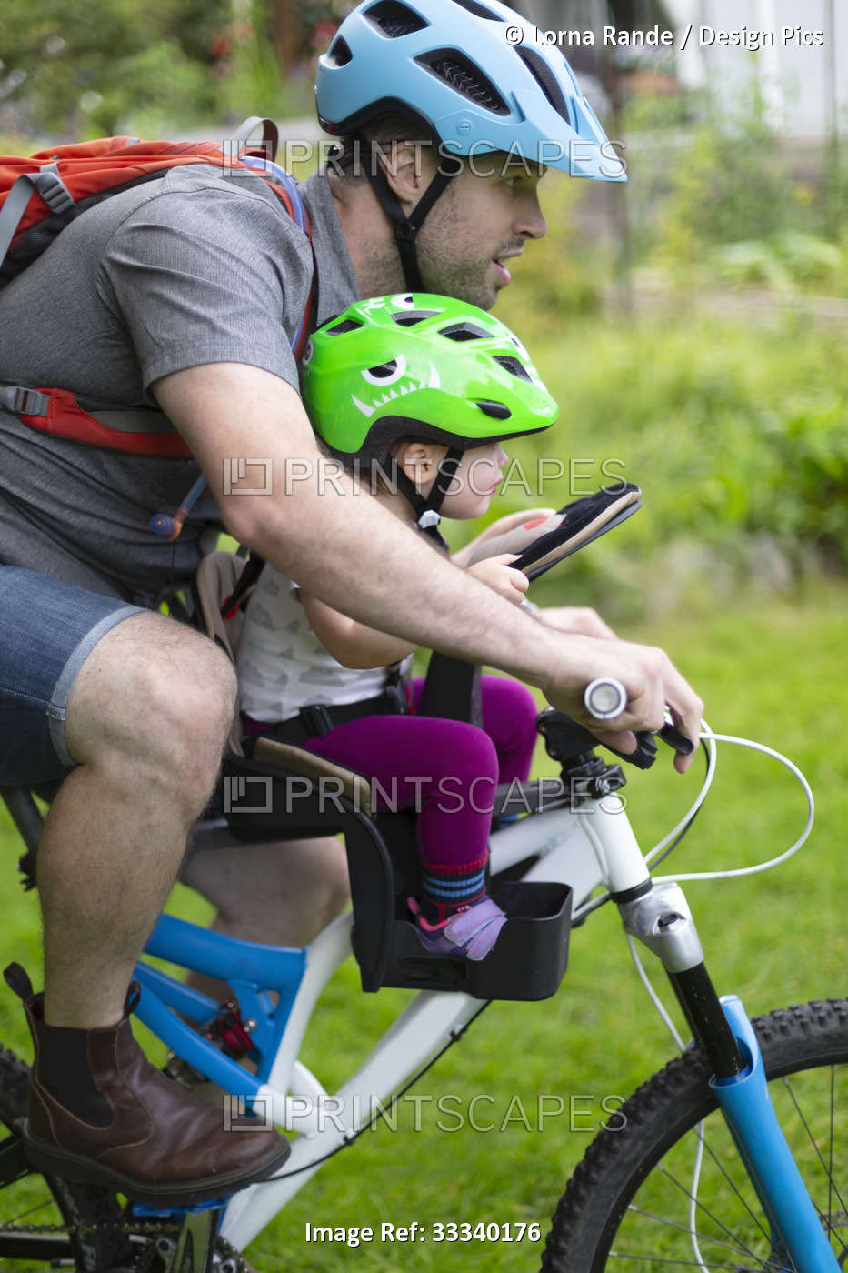 Father and young daughter ride together on a bike, the baby girl in a seat in ...
