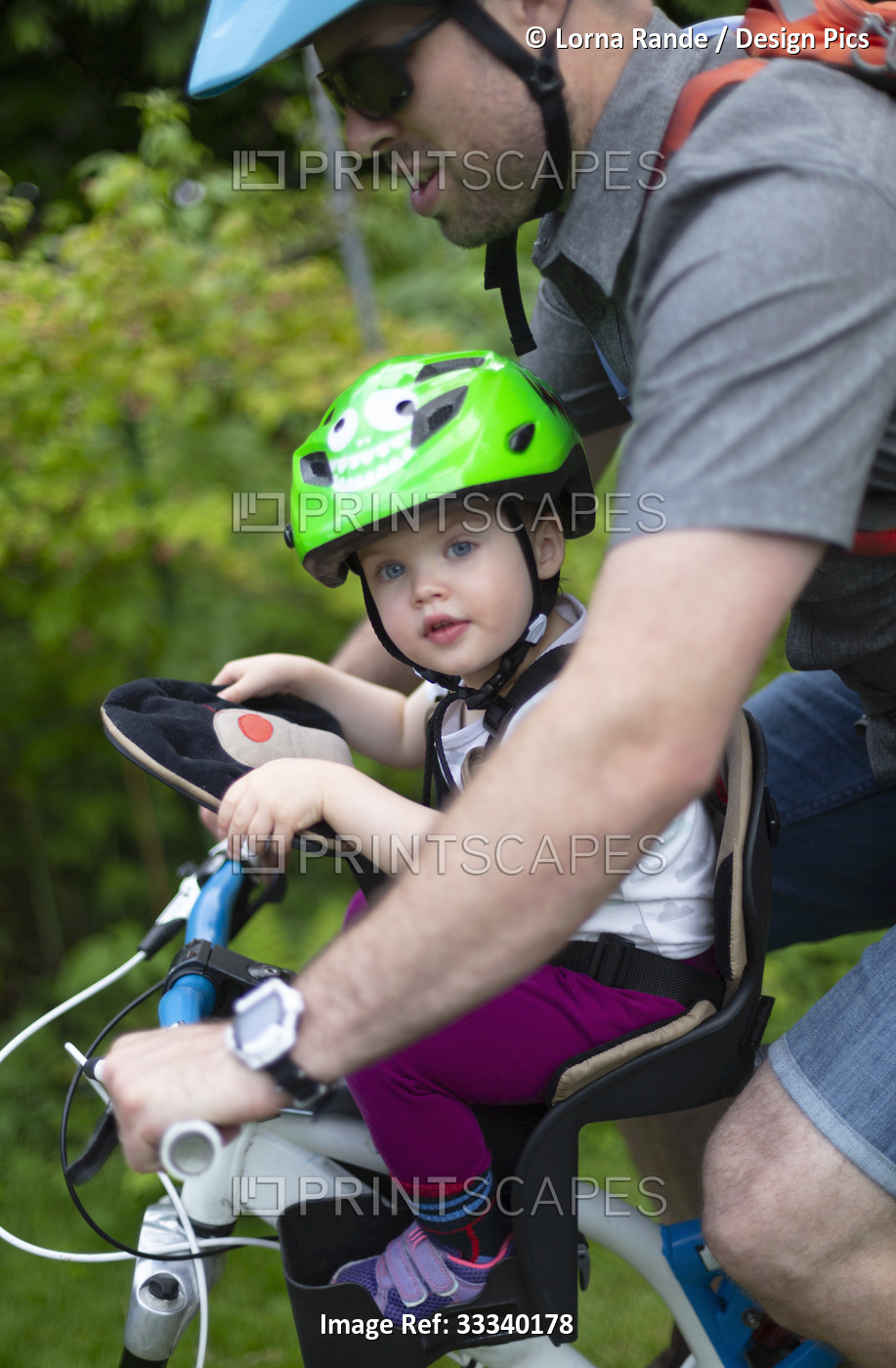 Father and young daughter ride together on a bike, the baby girl in a ...