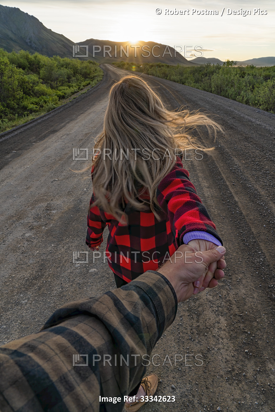 Man holding woman's hand as she leads them down a dirt road into the sunset ...