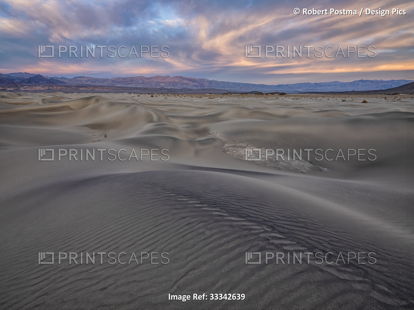 Sand dunes drifting in the foreground with a glowing sky at sunset over the ...