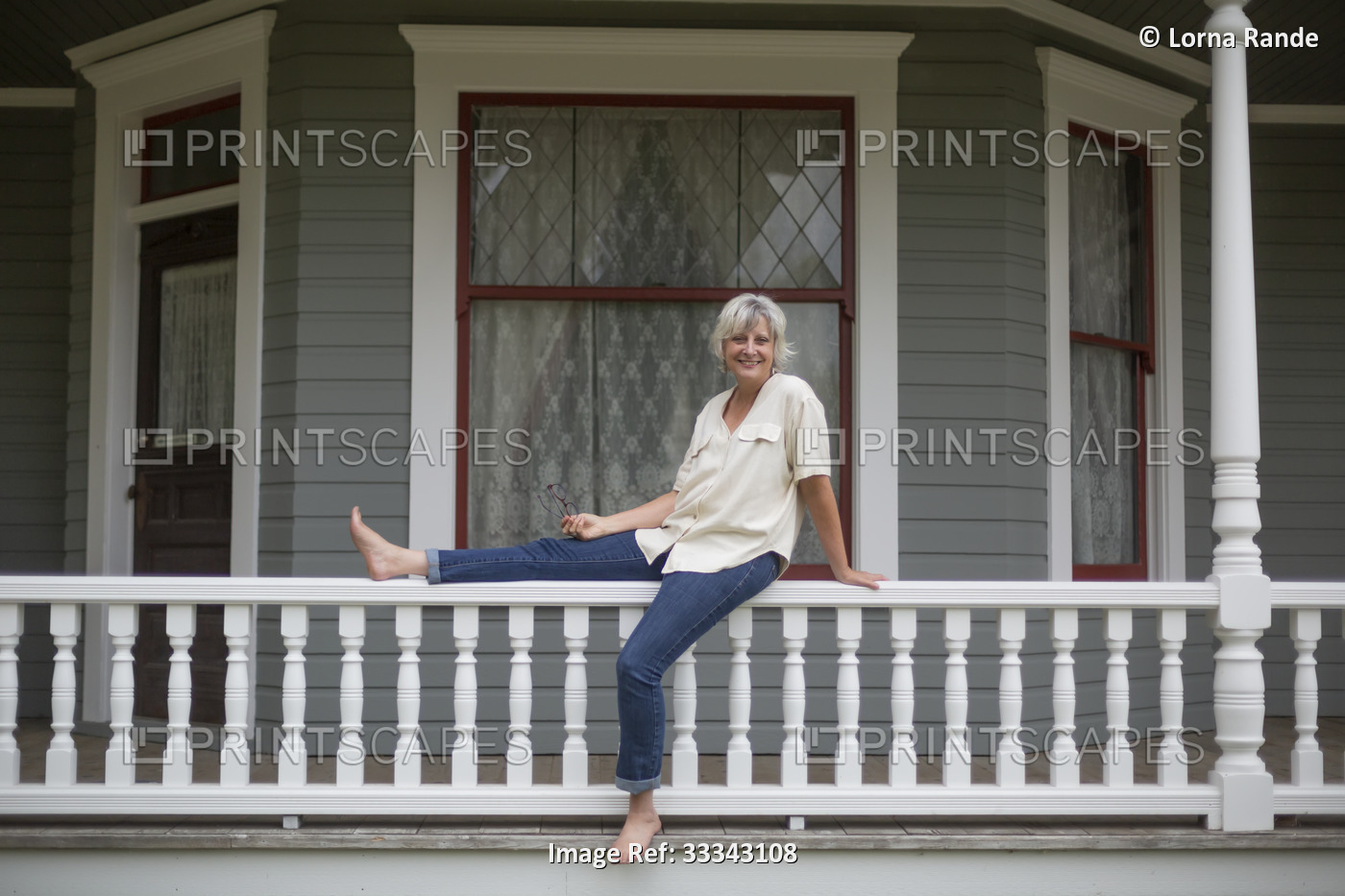 Portrait of a mature woman in casual clothing sitting on a porch railing at ...