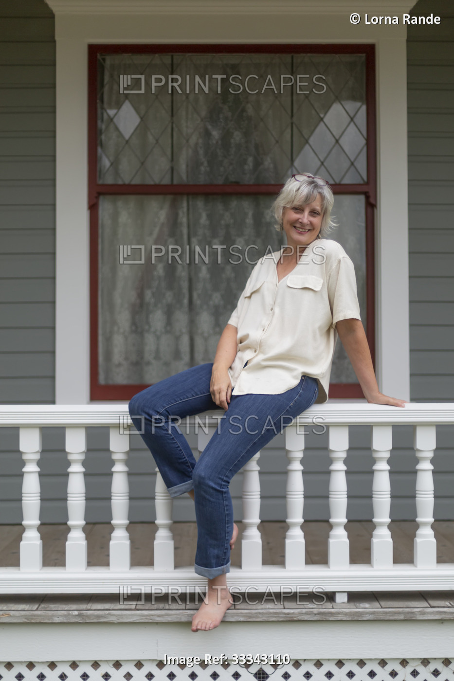 Portrait of a mature woman in casual clothing sitting on a porch railing at ...