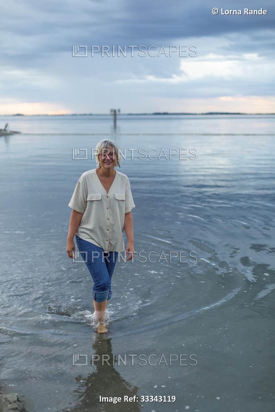 Woman wading in the water close to the shore, smiling and looking at camera; ...