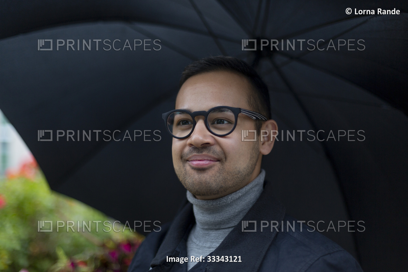 Close-up portrait of a man wearing eyeglasses standing under an umbrella ...