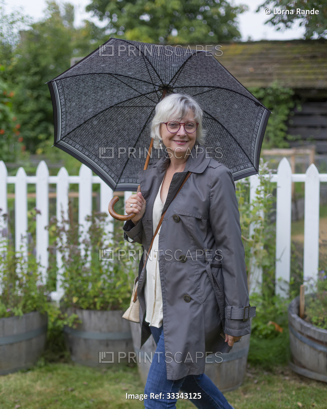 A mature woman walking in a neighbourhood with an umbrella; Surrey, British ...