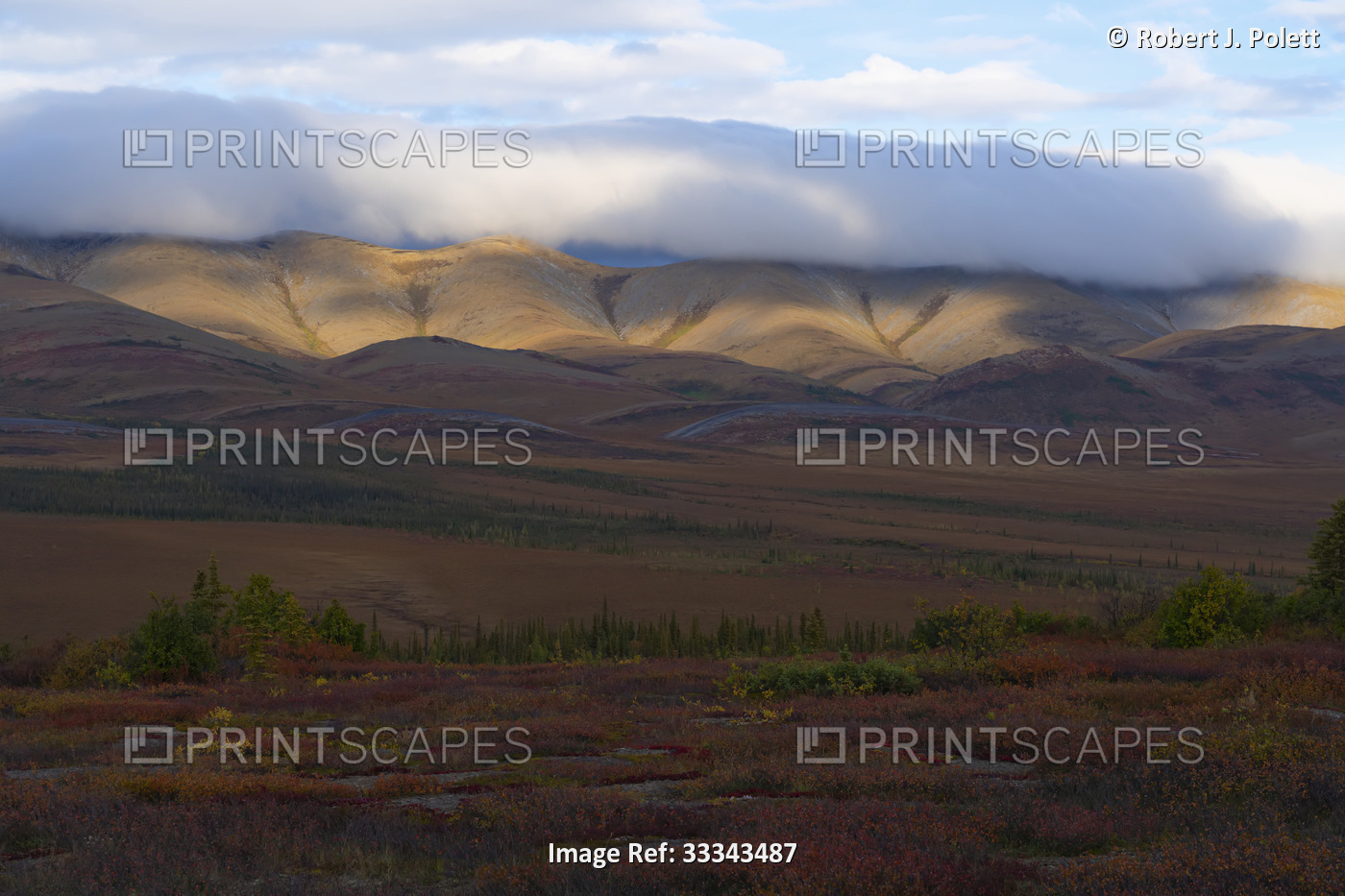 Scenic overview of the tundra and sunlit mountains along the Dempster Highway ...