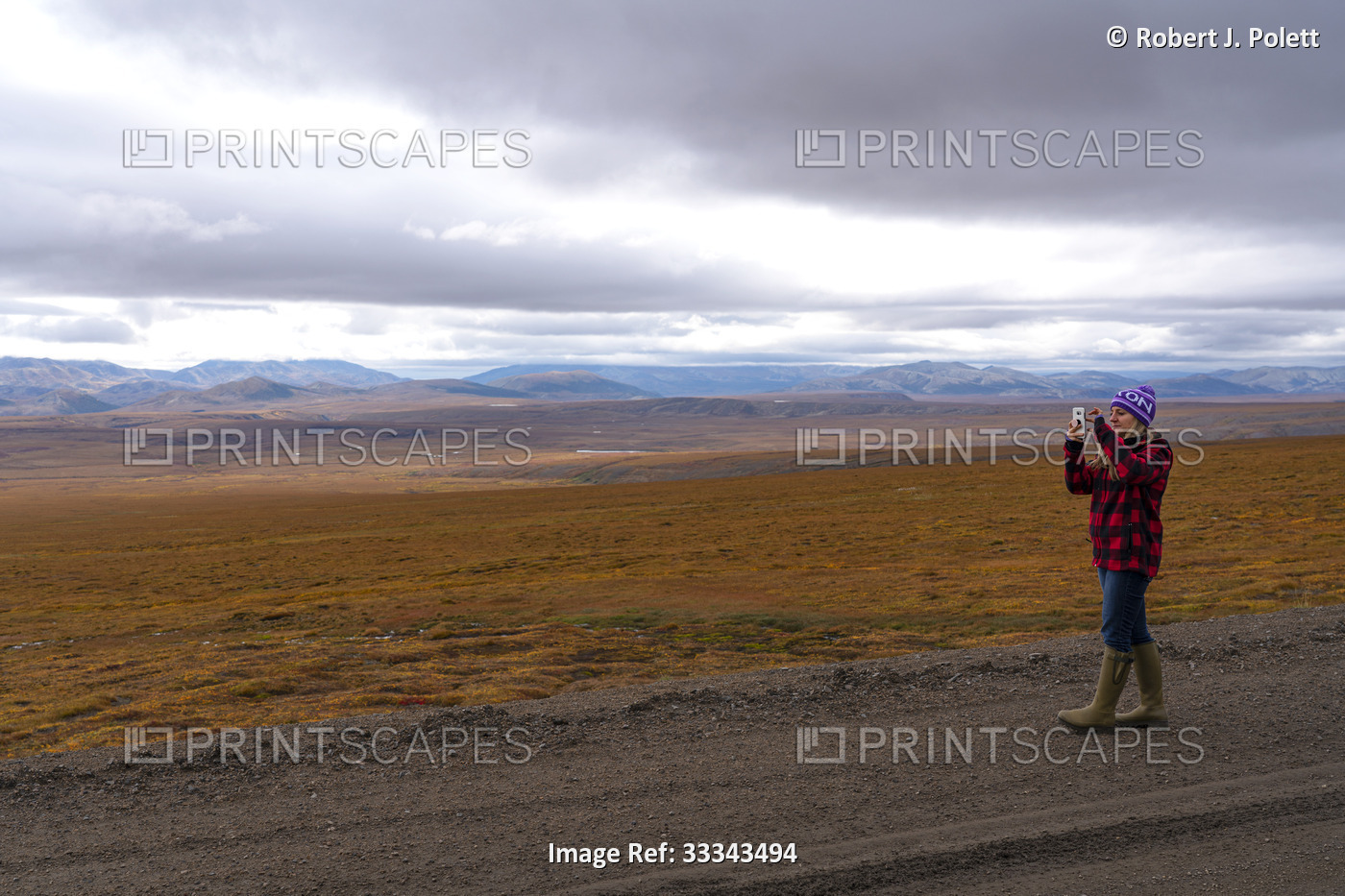 Woman traveler standing on gravel road taking photos of the vast, fall colored  ...
