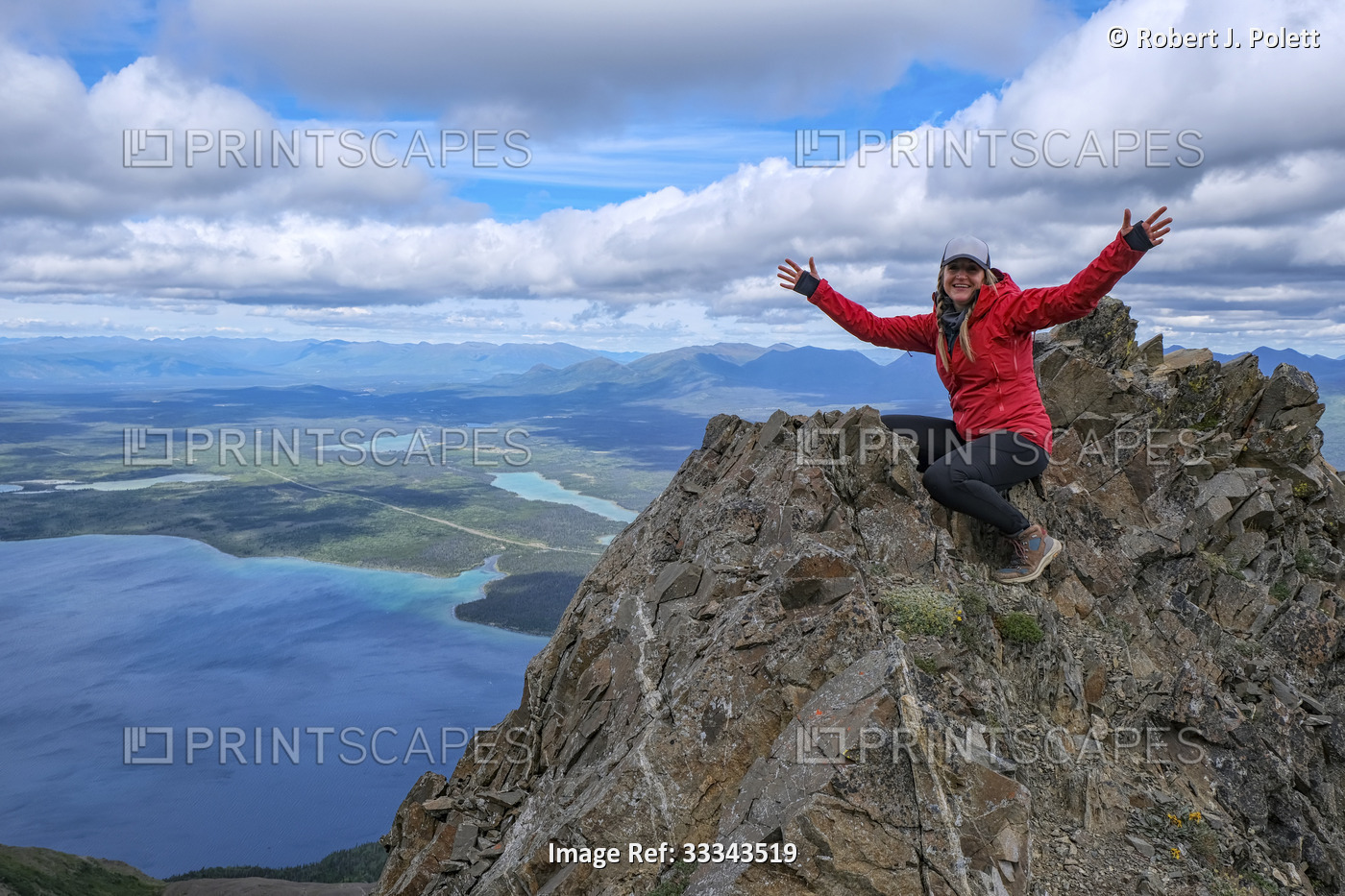 Woman sitting on top of a craggy mountaintop with arms outstretched and smiling ...