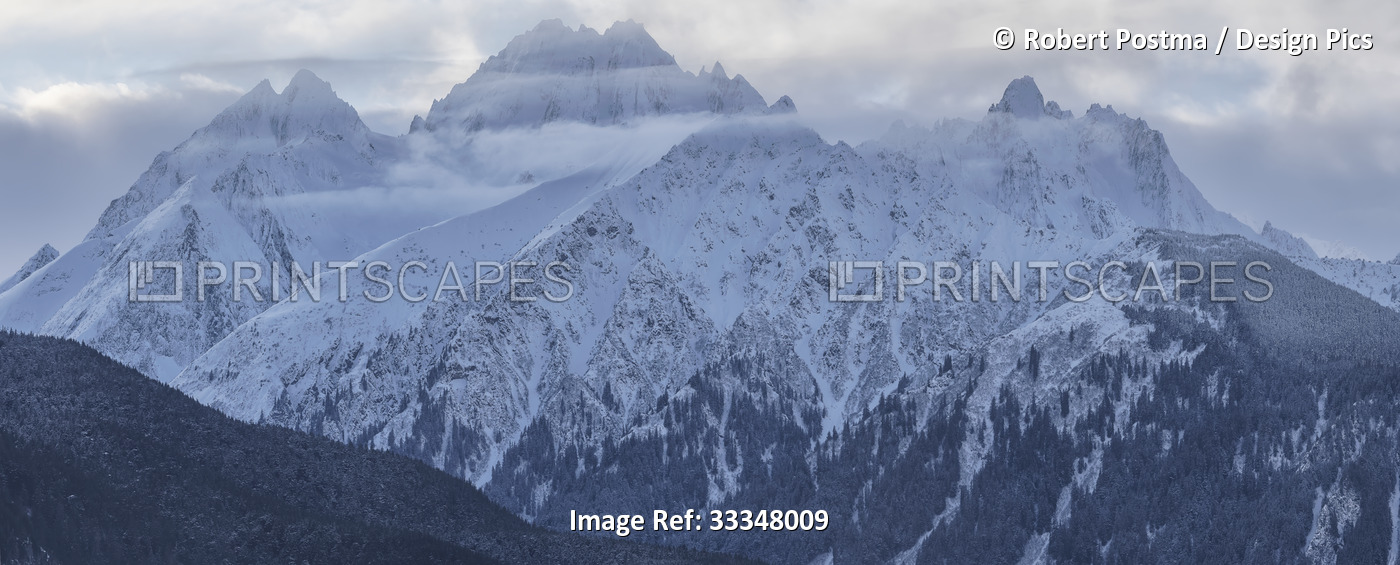 Snow covered majestic mountains with misty clouds hovering at the peaks; ...