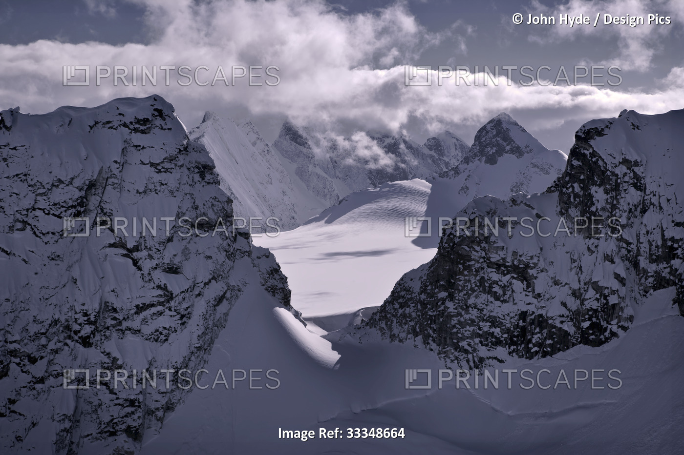 Snow covered jagged mountain peaks with a purple-grey hue surrounding the ...