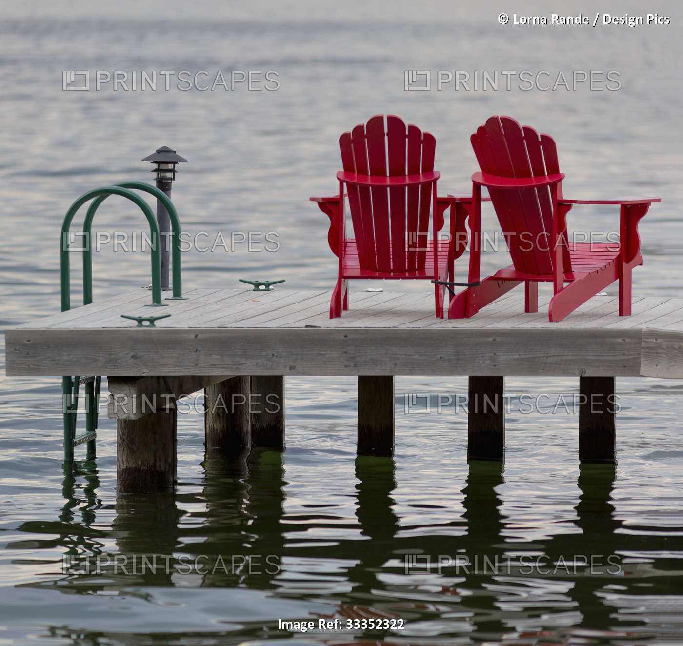 Two red adirondack chairs on a dock on Okanagan Lake; Peachland, British ...