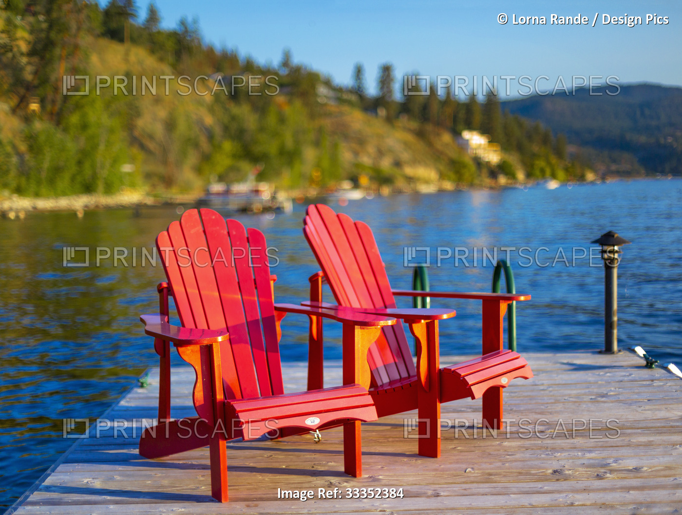 Two Adirondack chairs sit on a wooden dock on Okanagan Lake at sunset; British ...