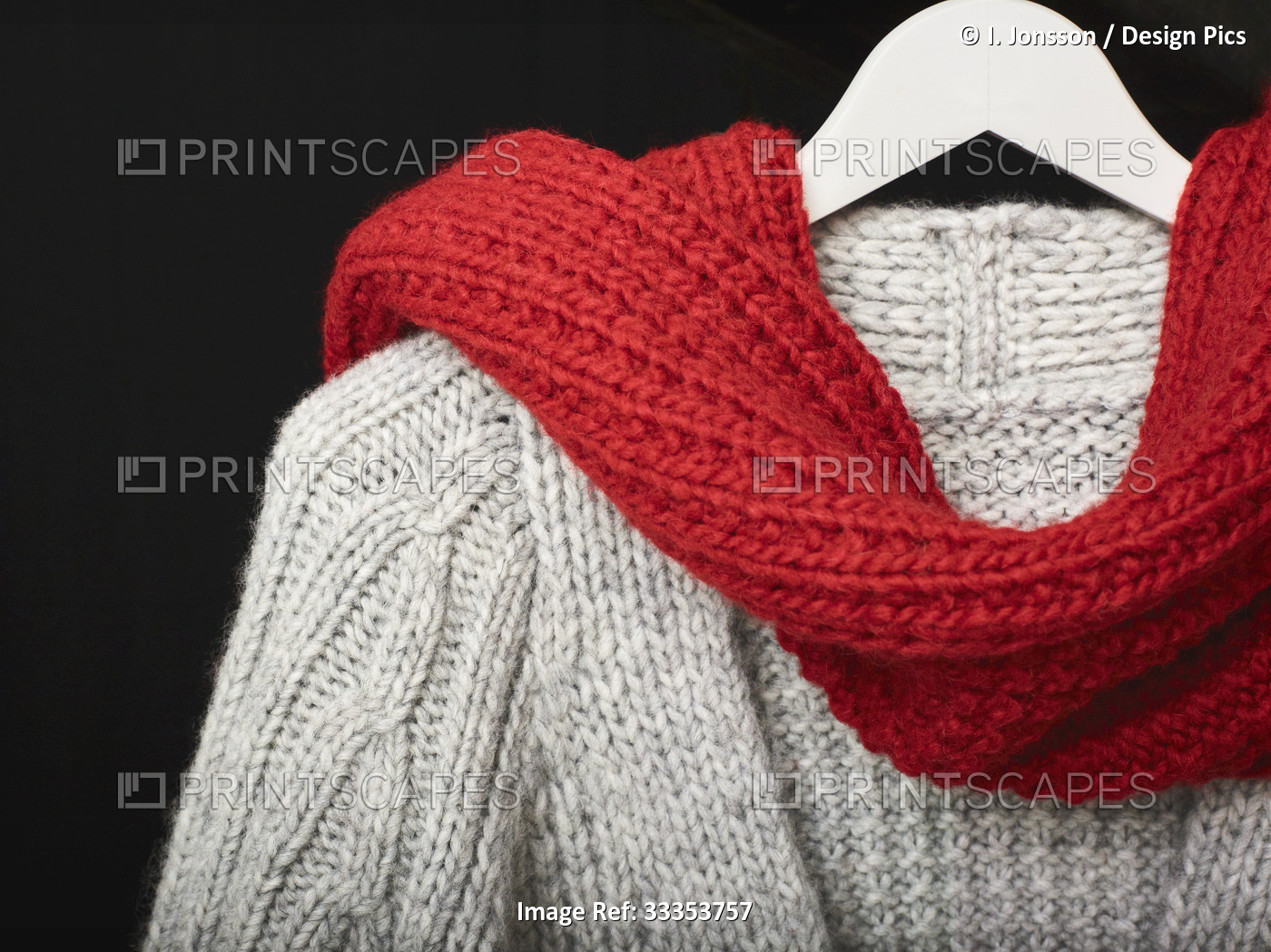 A grey knit sweater draped with a red knit scarf displayed on a hanger on a ...