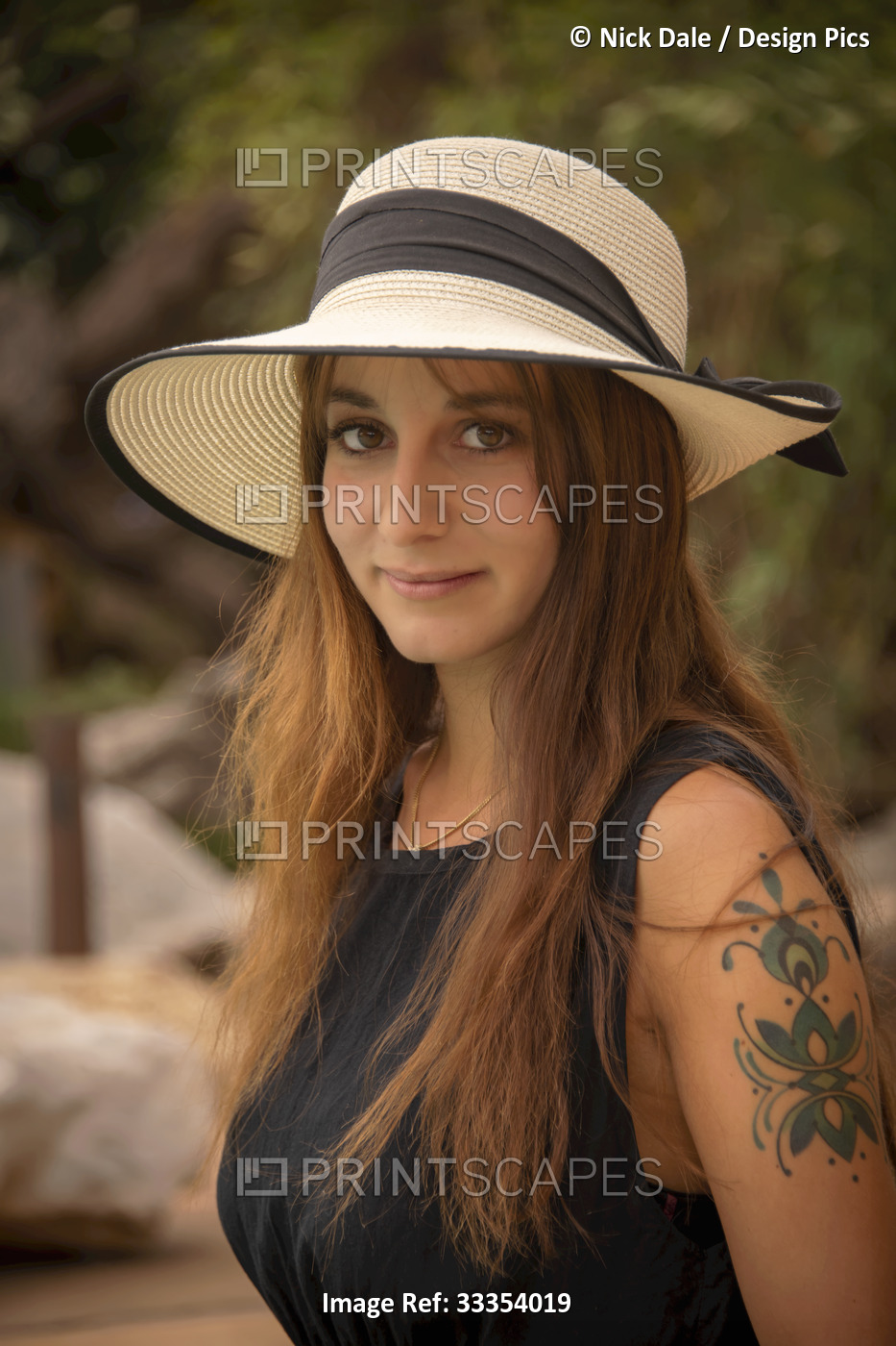 Close-up portrait of woman with a tattoo on her arm wearing a straw hat and ...